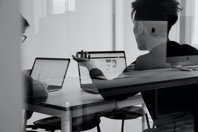 How Do I Choose A Virtual Assistant Two person sitting at a table in an office and working on their laptops.